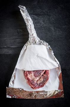 a piece of meat wrapped in foil on top of a black surface with a knife sticking out of it