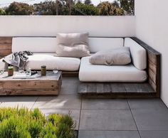 a white couch sitting on top of a patio next to a wooden table and potted plants