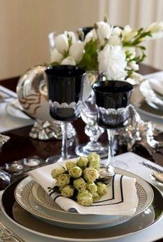 the table is set with black and white dishes, silverware, and flowers in vases