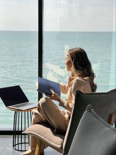 a woman sitting on a chair looking out at the ocean