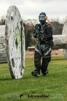 a man in black and green gear standing next to a large tire on the grass