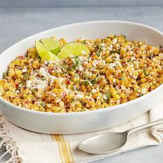 a white bowl filled with corn and topped with a lime wedge next to a fork