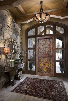 a foyer with stone walls and wooden doors, rugs on the floor and chandelier