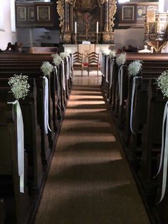 rows of pews decorated with white flowers and ribbons in front of an ornate mirror