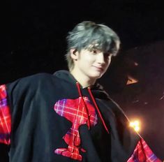 a young man with grey hair wearing a black shirt and red plaid cape on stage