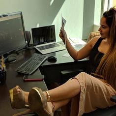 a woman sitting at a desk with her feet up in the air while reading a book