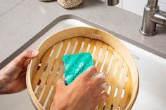 a person cleaning a sink with a sponge and a green cloth on the bottom of it