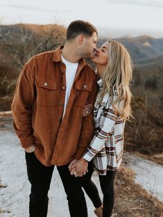 a man and woman kissing while standing on top of a hill