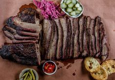 a large steak is cut into pieces and served with pickles, olives, and bread