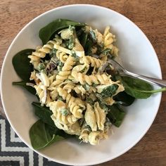 a white bowl filled with pasta and spinach on top of a wooden table next to a black and white rug