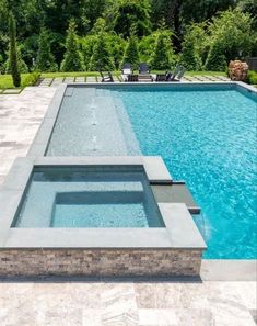 an empty swimming pool surrounded by greenery and trees in the background is a patio with lounge chairs