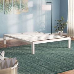 a white bed frame sitting on top of a wooden floor next to a green rug