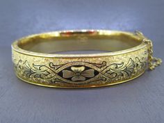 Gorgeous Victorian revival piece from the 1930s: a beautiful 12k gold filled bangle bracelet with floral detailing traced with black enamel.    Clasp works great and has a safety chain.  Marked 1/20th 12k Gold Filled Hayward. Visit Ribbons Edge for more great pieces of vintage and antique jewelry!  All items added to your cart at Ribbons Edge will automatically combine shipping. To stay up to date with my newest offerings, follow me on IG @ RibbonsEdge Antique 14k Stamped Bangle As Gift, Yellow Gold Art Deco Bracelet, Heirloom 14k Stamped Jewelry Bangle, Vintage Yellow Gold Bangle Stamped 14k, Art Deco Yellow Gold Wedding Bracelet, Vintage Yellow Gold Hallmarked Cuff Bracelet, Vintage Yellow Gold Hinged Bracelet, Vintage Gold Bangle Bracelet With 17 Jewels, Victorian Yellow Gold Hinged Jewelry