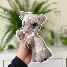 a person holding up a small stuffed cat