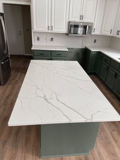 a kitchen with white marble counter tops and green cabinetry in the center, along with stainless steel appliances