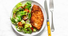 a white plate topped with meat and salad next to a fork on top of a table