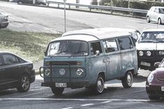 an old vw bus is driving down the street with other cars in traffic behind it