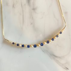 a gold necklace with blue and white pearls on it's side, sitting on a marble surface