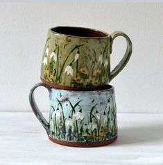 two mugs sitting side by side on a white counter top with flowers painted on them