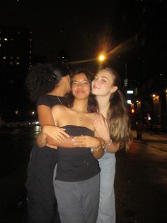 three women hugging each other on the street at night