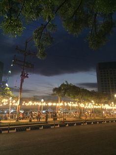 people are standing on the side of the road at night with lights strung across the street