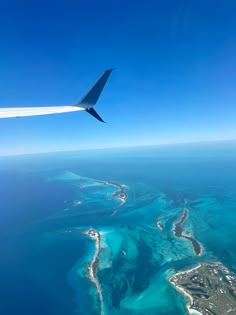 an airplane wing flying over the ocean and coral reef landforms in the water below