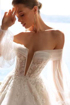 a woman in a wedding dress is holding her hand up to her face and looking down