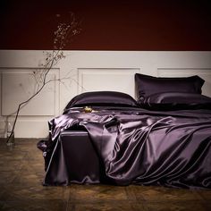 a bed with purple sheets and pillows on top of wooden floor next to white paneled wall