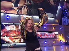 the man is holding his arms in the air while standing on stage with two snakes around his neck