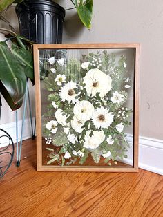 a wooden frame with flowers in it sitting on the floor next to a potted plant