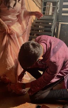 a man kneeling down next to a woman in a pink dress