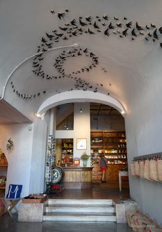 birds are flying in the air above a store front entrance with stairs leading up to it