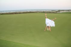 a person jumping in the air on top of a grass covered field next to the ocean