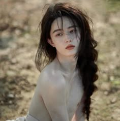 a naked woman sitting on the ground with her hair blowing in the wind and looking at the camera