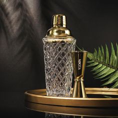 a glass bottle with a golden top on a tray next to a fern leaf and a gold cup