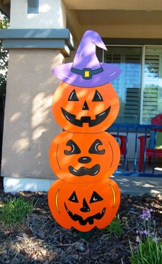 three pumpkins stacked on top of each other in front of a house with a witch hat