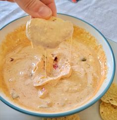 a person dipping tortilla chips into a bowl of quesadilla dip