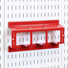 a red shelf mounted to the side of a white wall with three holes in it