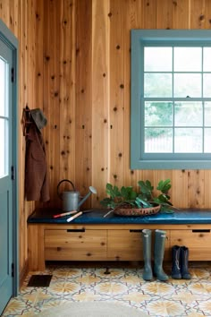 a wooden bench sitting in front of a window next to a pair of rubber boots