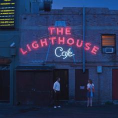 two people standing in front of a building with the words the lighthouse cafe on it