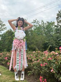 a woman is standing in the grass with flowers and ribbons around her neck, wearing converses