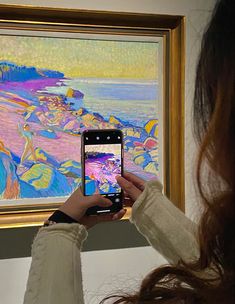 a woman taking a photo of a painting with her cell phone