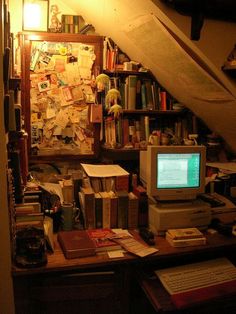 a computer sitting on top of a desk under a slanted ceiling next to a bookshelf