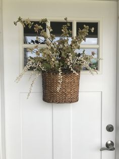 a basket with flowers hanging from the side of a door on a white front door