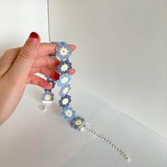 a hand holding a bracelet made out of crochet flowers and beads on a white surface