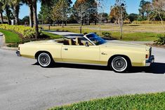 an old yellow convertible car parked on the side of the road in front of some palm trees