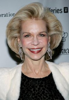 an older woman with blonde hair and earrings smiles at the camera while wearing a black dress