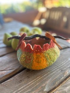 an orange, yellow and green bowl sitting on top of a wooden table next to apples