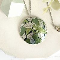 two necklaces with green leaves on them sitting next to some white and gray flowers