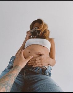 a man is holding a woman's belly while she takes a photo with her camera